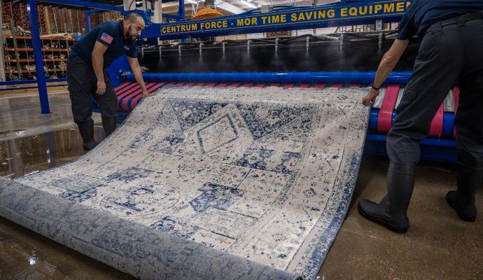 two individuals cleaning blue and white patterned rug