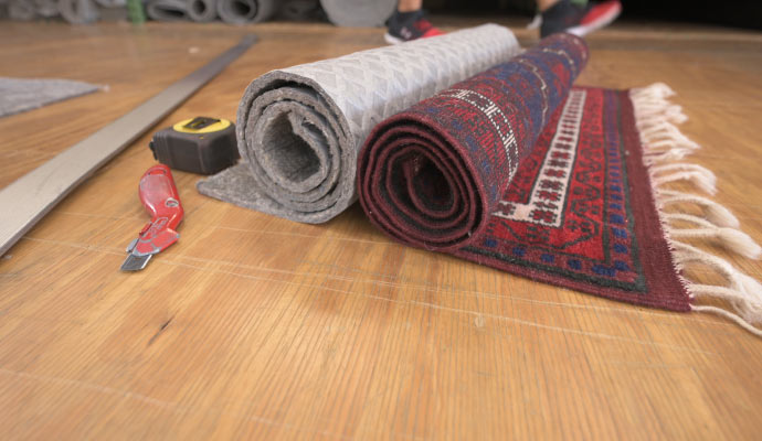 A rolled rug and rolled rug pad placed on wooden floor.