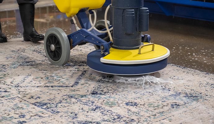 A person using a professional rug scrubber to clean a large, intricate rug 