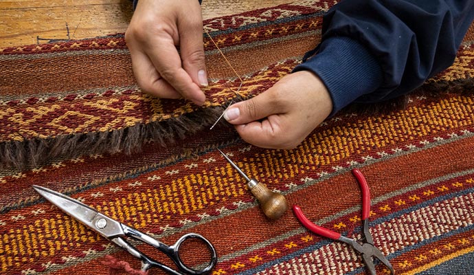 a person reweaving a colorful rug with rug rapair tools